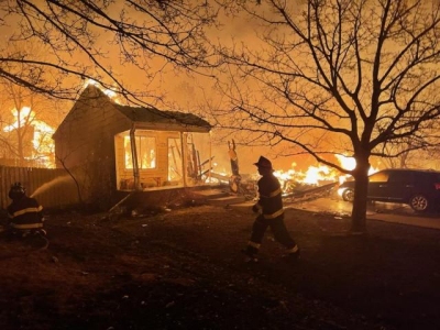 Denver firefighter approaches a small structure consumed by a firey blaze